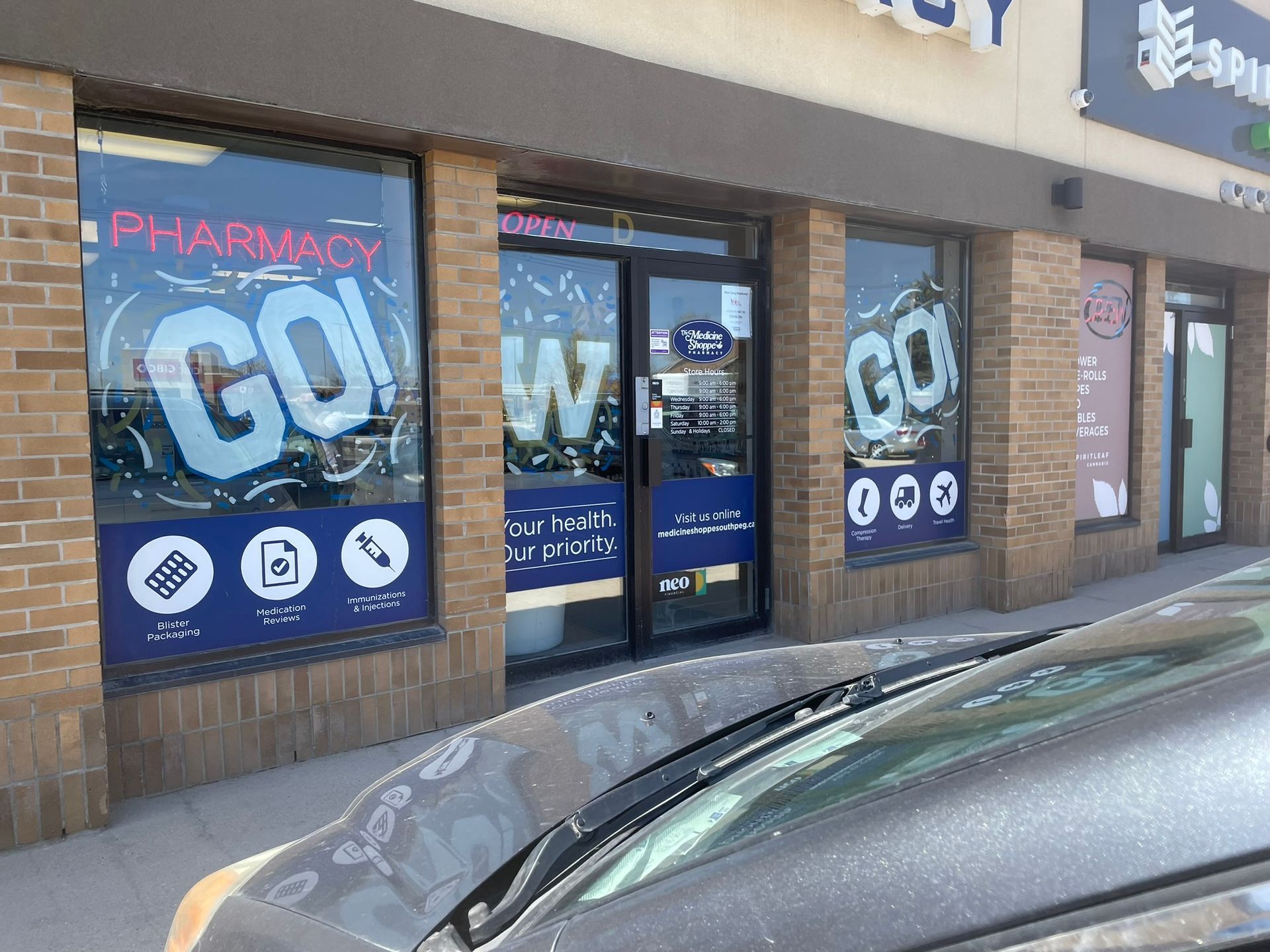 A pharmacy with a car parked in front of it.