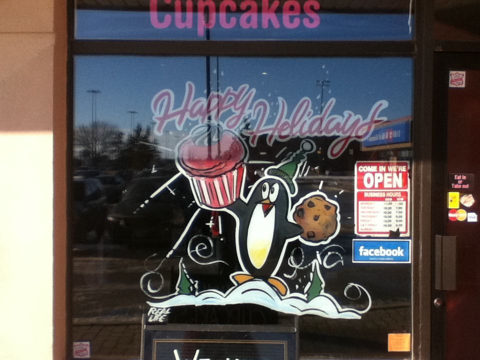 A window with a penguin holding a cupcake and a cookie