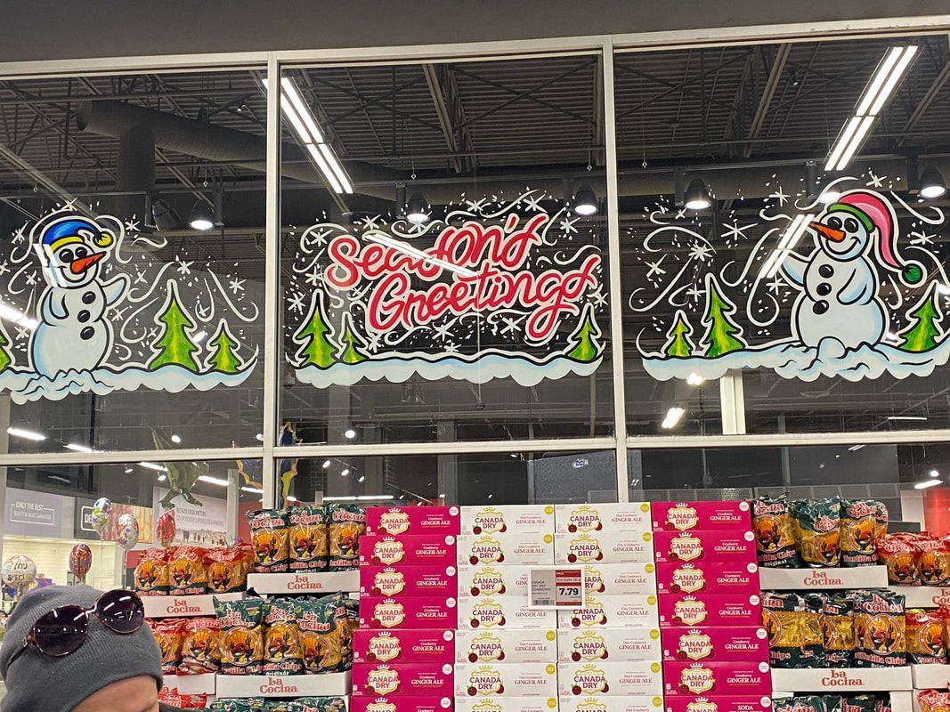 A man is standing in front of a store window with christmas decorations on it.