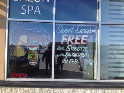 A window with a sign that says sweet escapes free peg smoothie with salon visit in feb