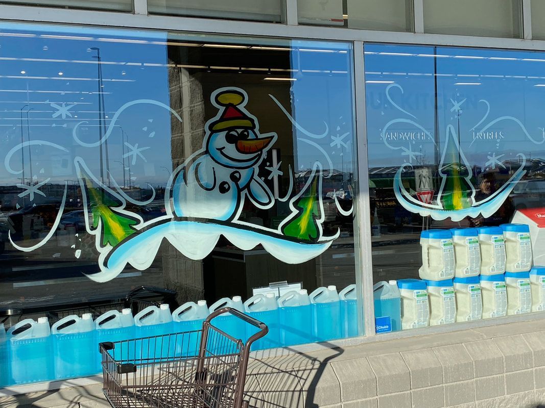 A shopping cart is parked in front of a store window with a snowman and christmas trees painted on it.