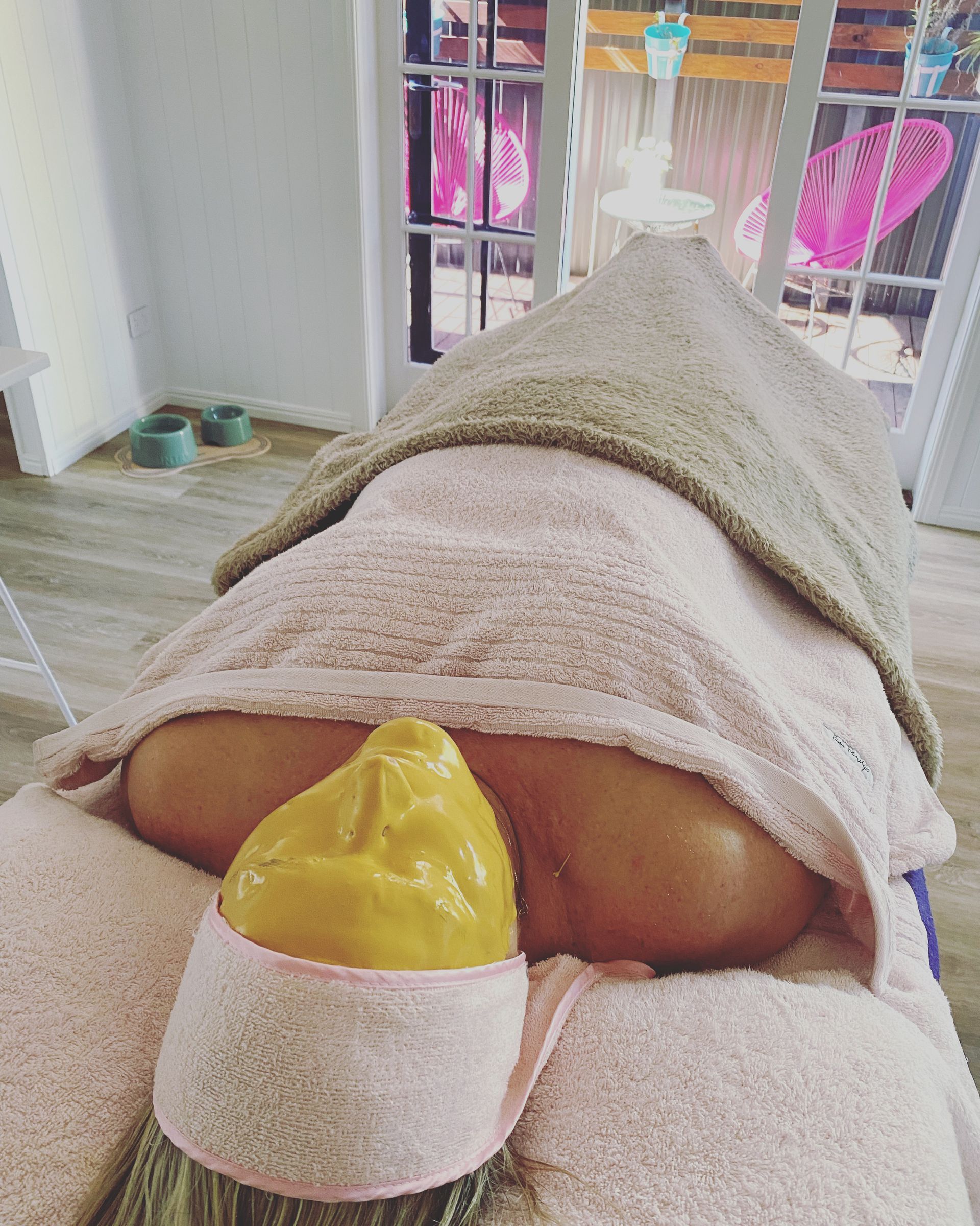 A person lying down with a facial yellow mask on in a spa setting — Soul Good Beauty in Miami, QLD