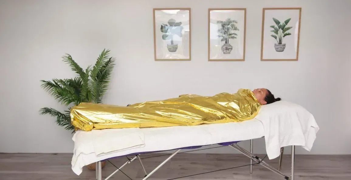 Person Wrapped in A Gold Blanket on A Massage Table — Soul Good Beauty in Miami, QLD