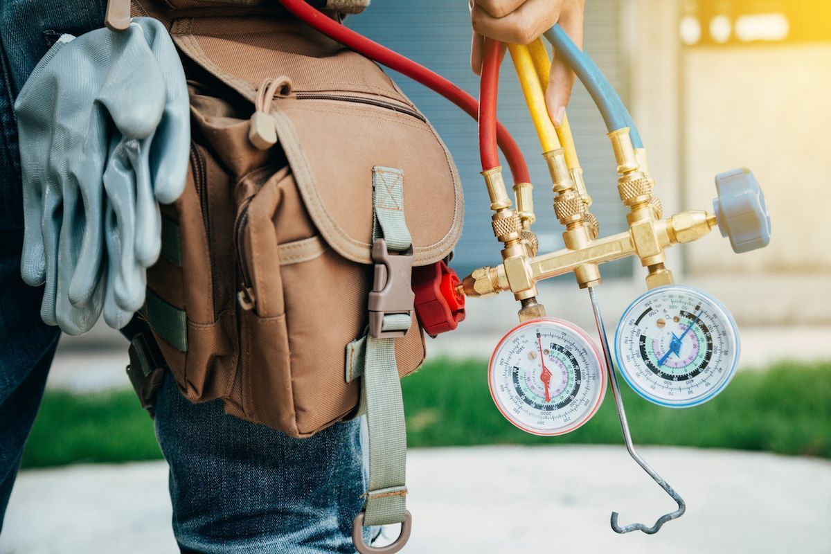 HVAC technician’s tool belt with gloves and manifold gauges attached to yellow and red hoses