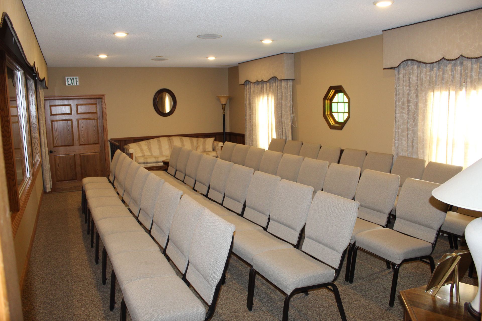 Rows of beige chairs face forward in a room. A table and staircase railing are in the foreground.