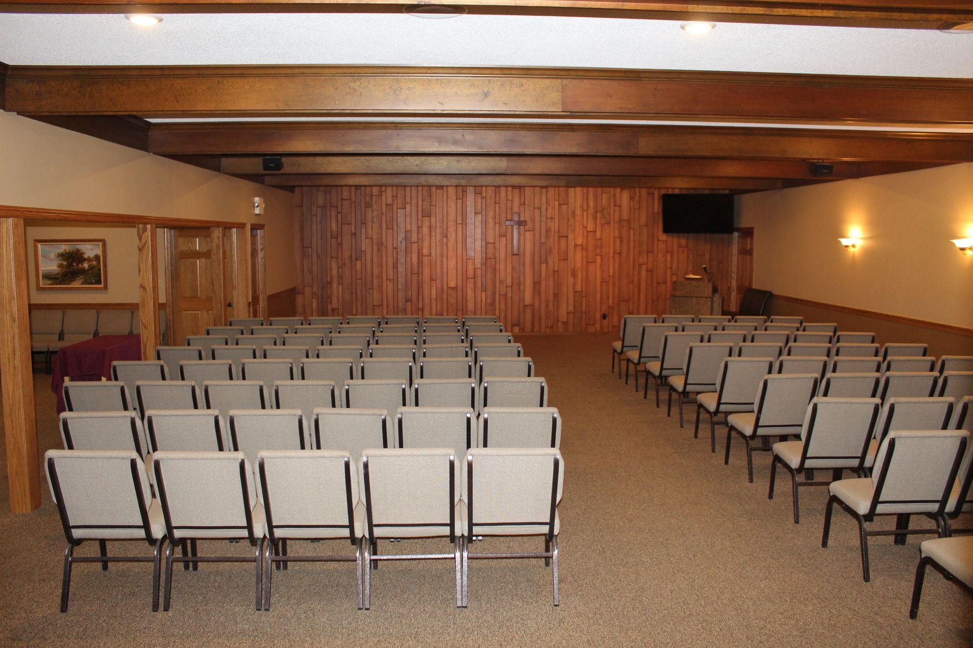 Rows of empty gray chairs in a wood-paneled church sanctuary, with a cross on the wall.