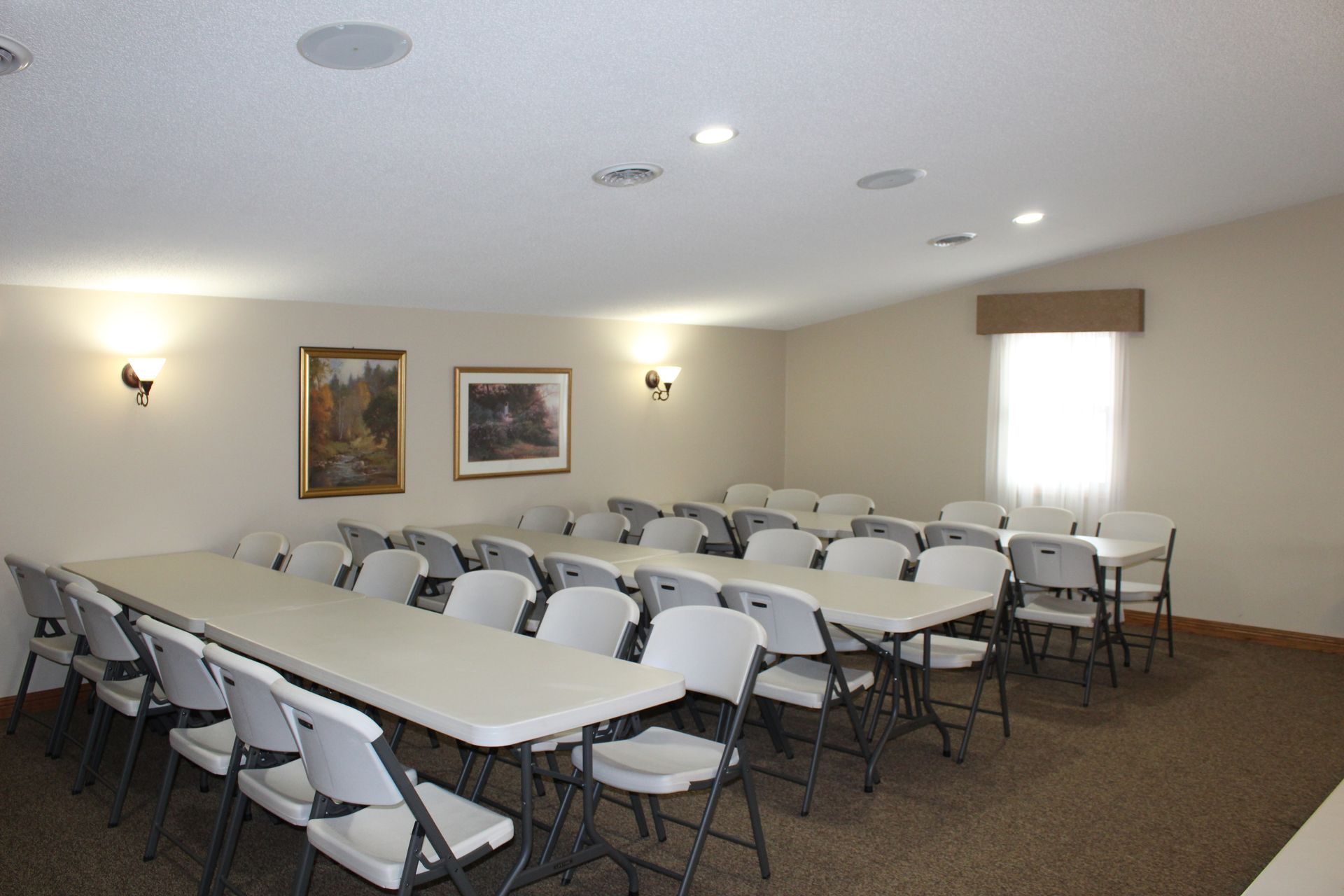 An empty event room with tables and chairs set up, light walls, brown carpet.