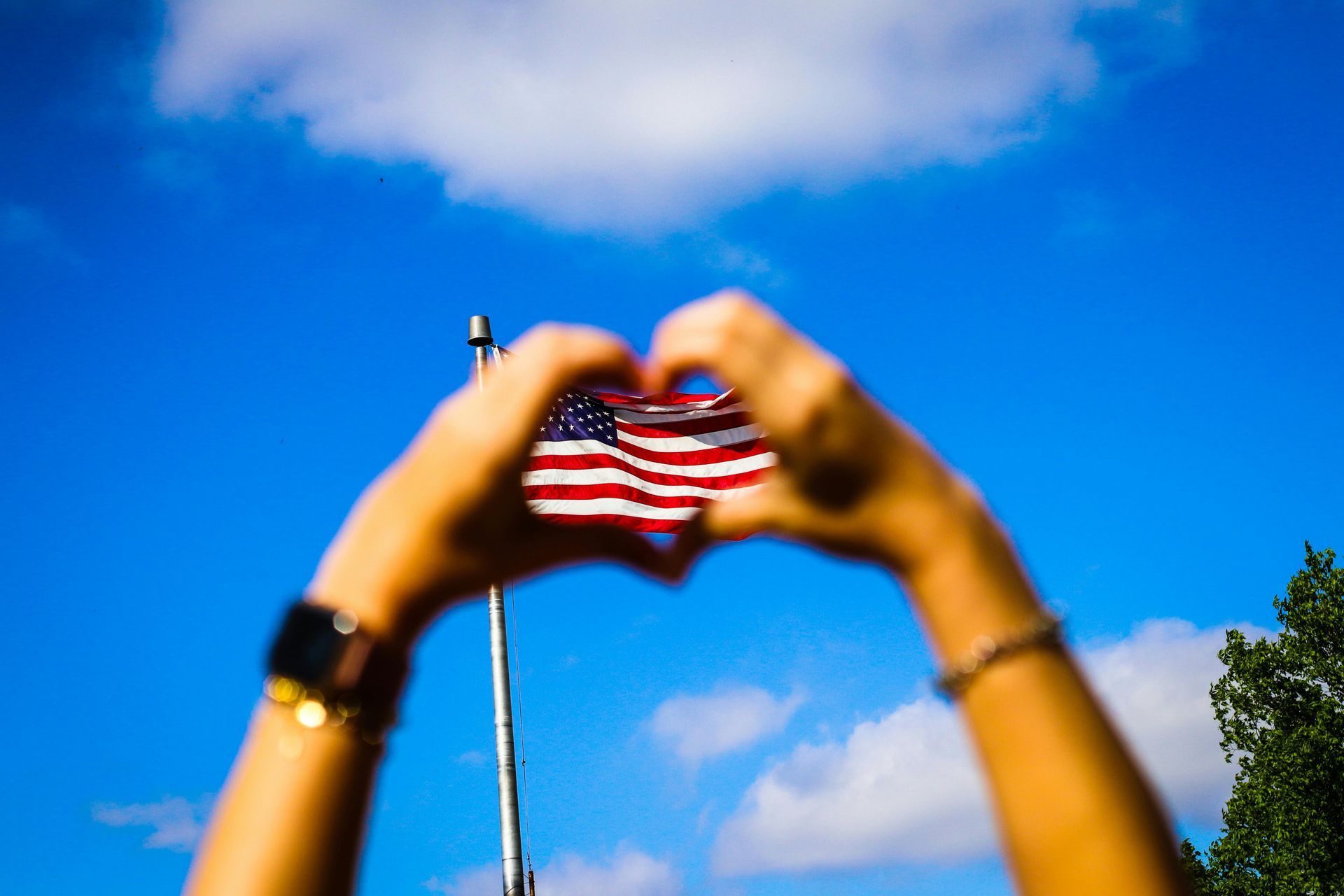 A person is making a heart shape with their hands in front of an american flag