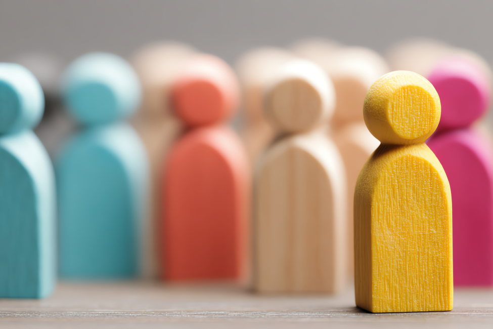 Wooden figurines, one yellow in front, others in various colors, blurred background.