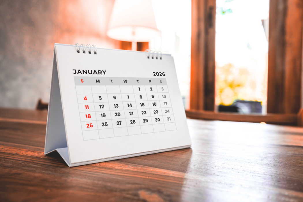 A white desk calendar open to January on a wooden table near a window.