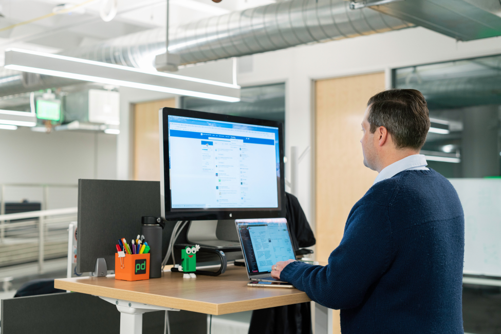 Person at an office desk using a laptop and large monitor in a modern workspace