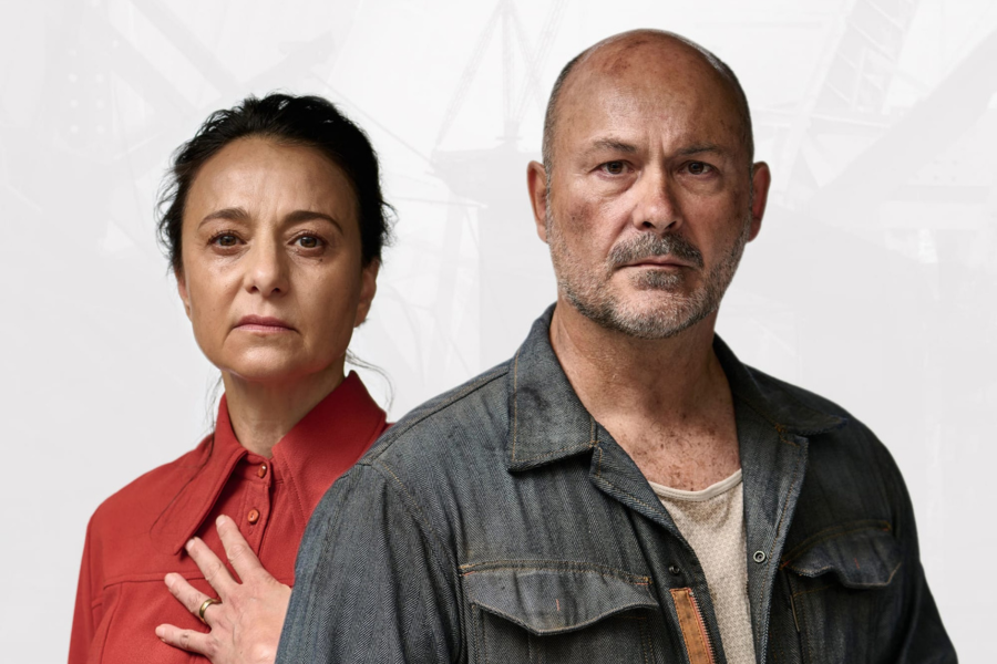 A woman in a red shirt and a man in a grey denim jacket stand side-by-side, both looking forward with serious expressions.
