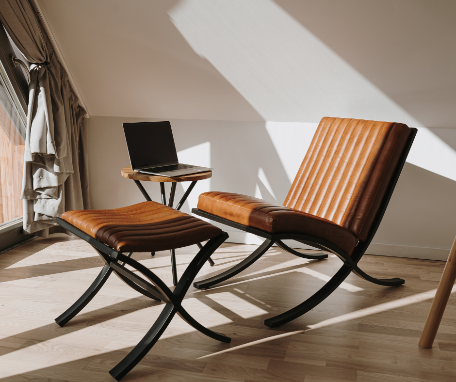 Leather chair and ottoman with a laptop on a small side table in a room with sunlight.