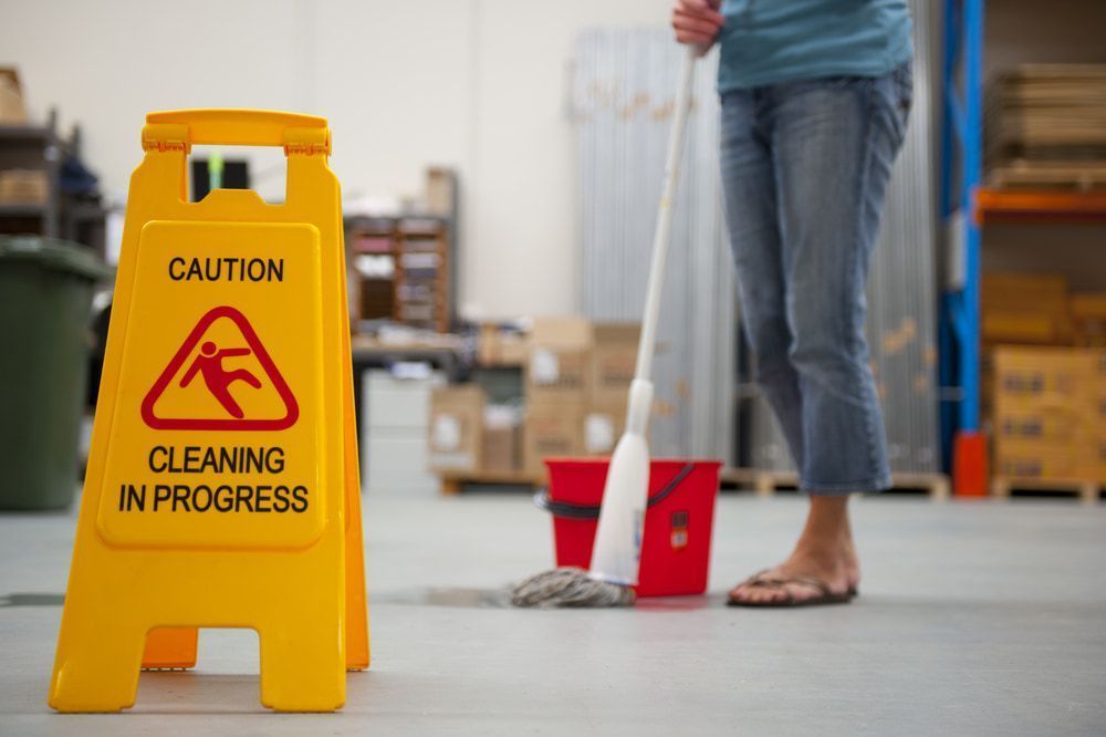 Woman is Mopping the Floor in a Warehouse Next to a Caution Sign — Active Cleaning Service Rutherfor