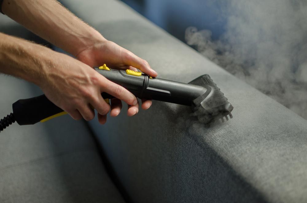 A person holding a steam brush cleaning a couch — Active Cleaning Service Maitland, NSW