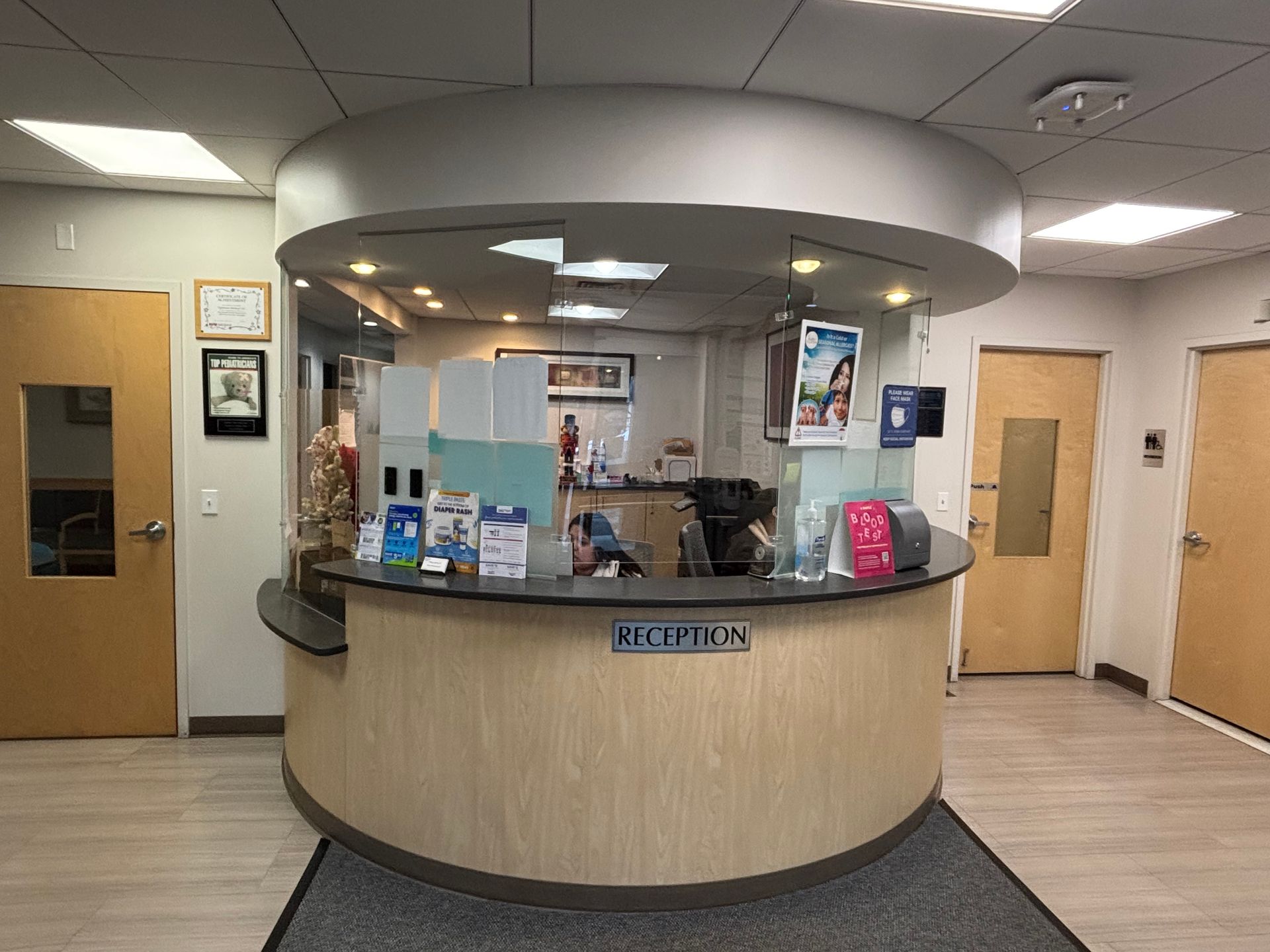 Reception desk in a clinic, light wood and gray hues, with curved counter and overhead circular design.
