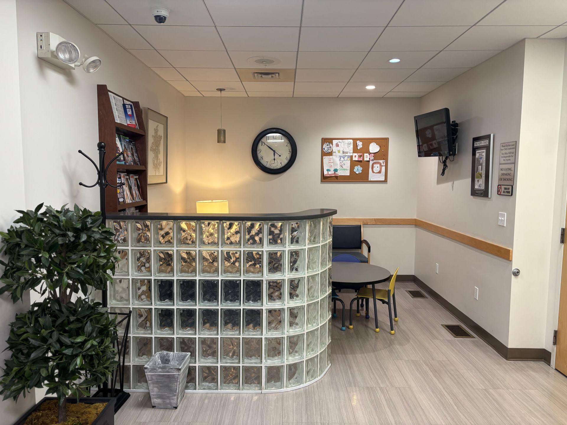 Reception area with glass brick counter, clock, TV, small table, and waiting chairs.