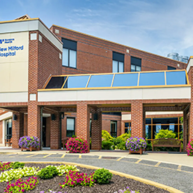 New Milford Hospital entrance; red brick building with covered walkway, flowers, and blue sky.