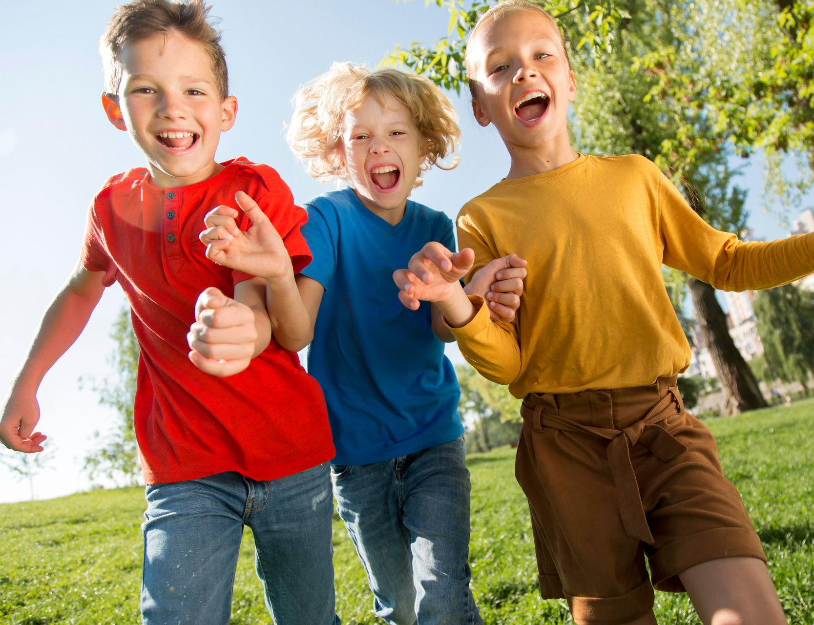Three children running and laughing in a park on a sunny day.