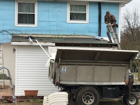 A man is working on the roof of a house next to a dump truck.
