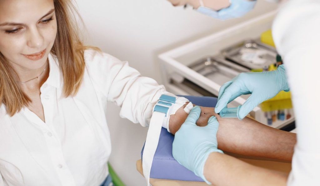 Woman having blood drawn in medical setting. Phlebotomist in gloves. Blue arm rest.