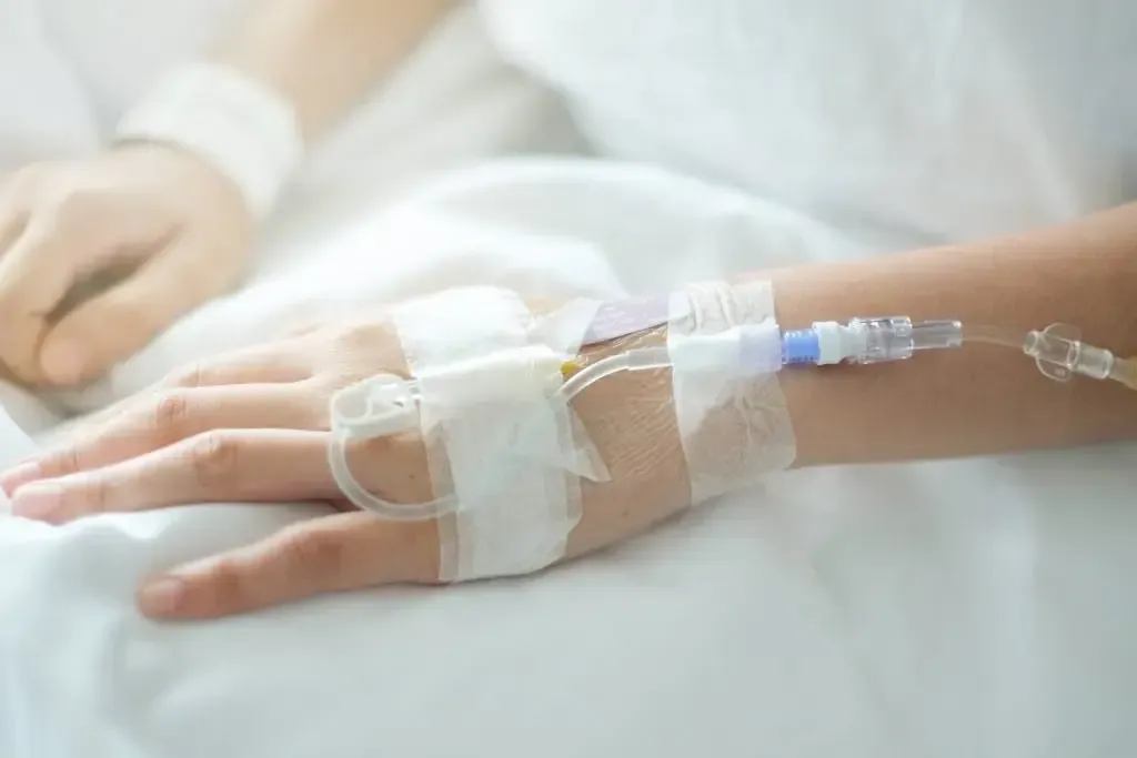 Hand with IV drip in a hospital bed, secured with white tape.