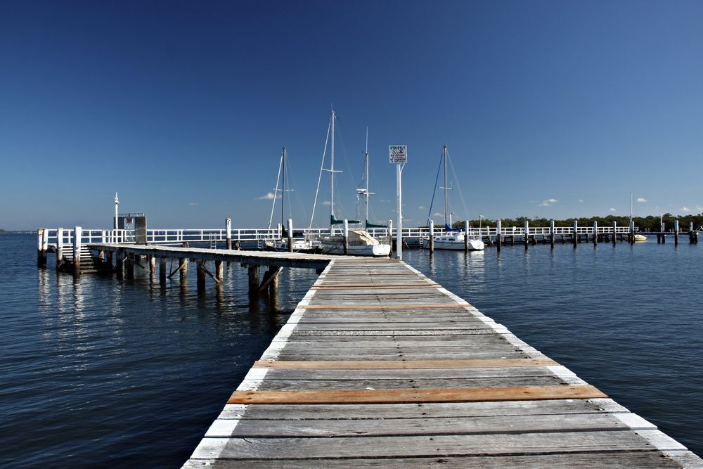 Wooden Dock Leading to a Marina With Sailboat — Aircon Mid North Coast in Port Stephens, NSW