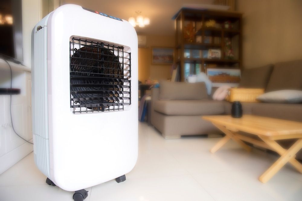 A White Air Cooler Is Sitting In A Living Room Next To A Couch — Aircon Mid North Coast in Forster, NSW