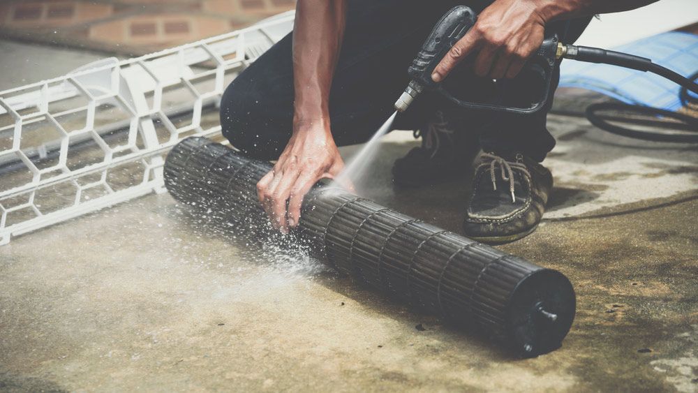 A Man Is Cleaning A Fan With A High Pressure Washer — Air Conditioning Electricians in Harrington, NSW