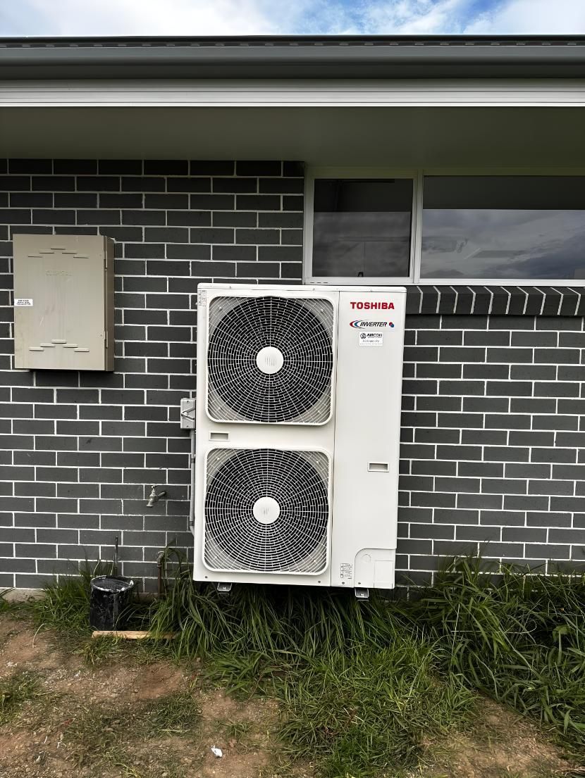 Large Air Conditioner is Mounted on the Side of a Brick Building — Air Conditioning Electricians in Forster, NSW