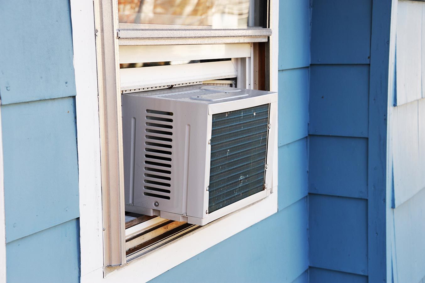 A Window Air Conditioner Is Installed In The Window Of A Blue House — Aircon Mid North Coast in Forster, NSW