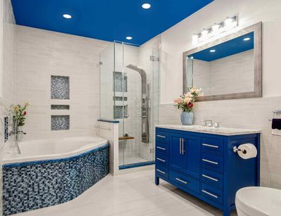 Blue and white modern bathroom with tub, shower, and vanity. Blue ceiling and mosaic details.