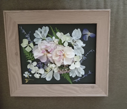Framed pastel floral arrangement with white and pink flowers, green leaves, and a dark background