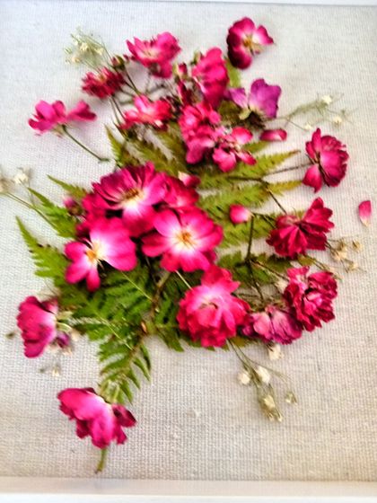 Pressed pink flowers arranged in a white shadow box on a wooden surface