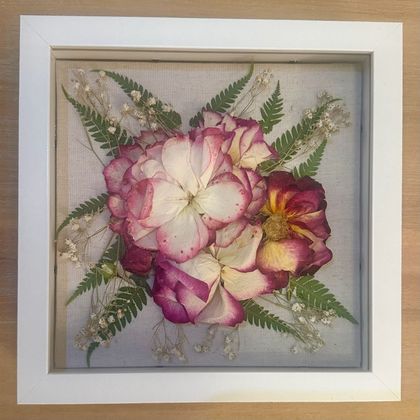 Framed floral arrangement with pink, white, and purple flowers and green fern leaves on a light background