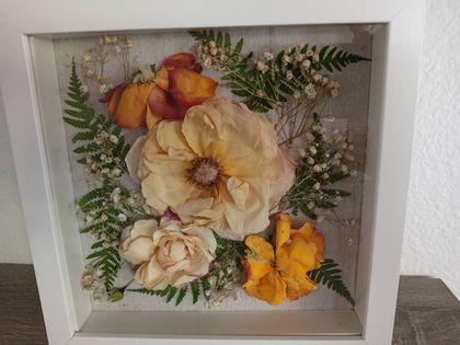 Framed floral arrangement with cream, orange, and yellow flowers and greenery