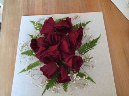 Bouquet of deep red roses with white filler flowers and green fern leaves on a white tablecloth