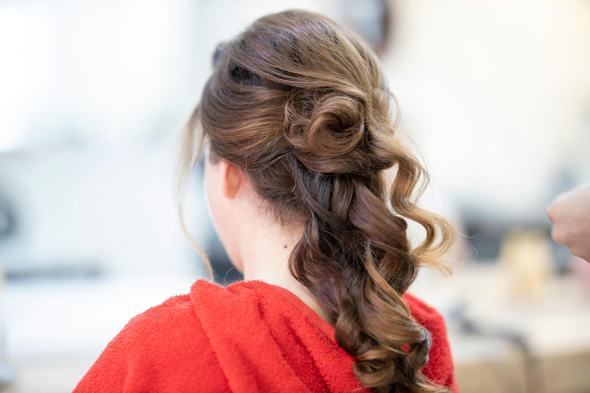 Woman with brown hair styled in an updo and loose curls, wearing a red top.