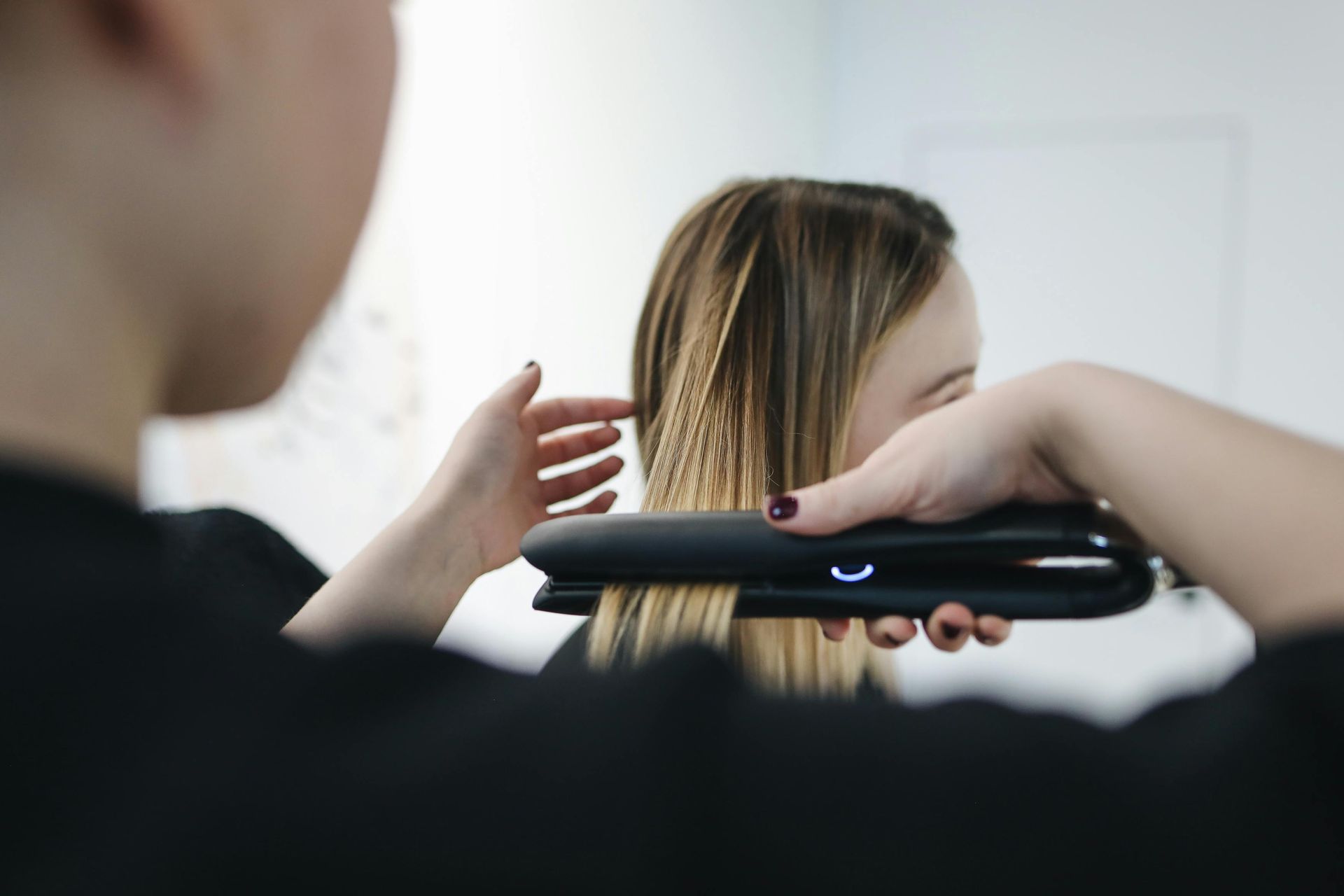 A person using a flat iron on another person's hair in front of a mirror.