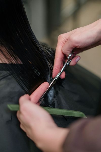 Hairdresser cutting wet, dark hair with scissors and a comb in a salon setting.