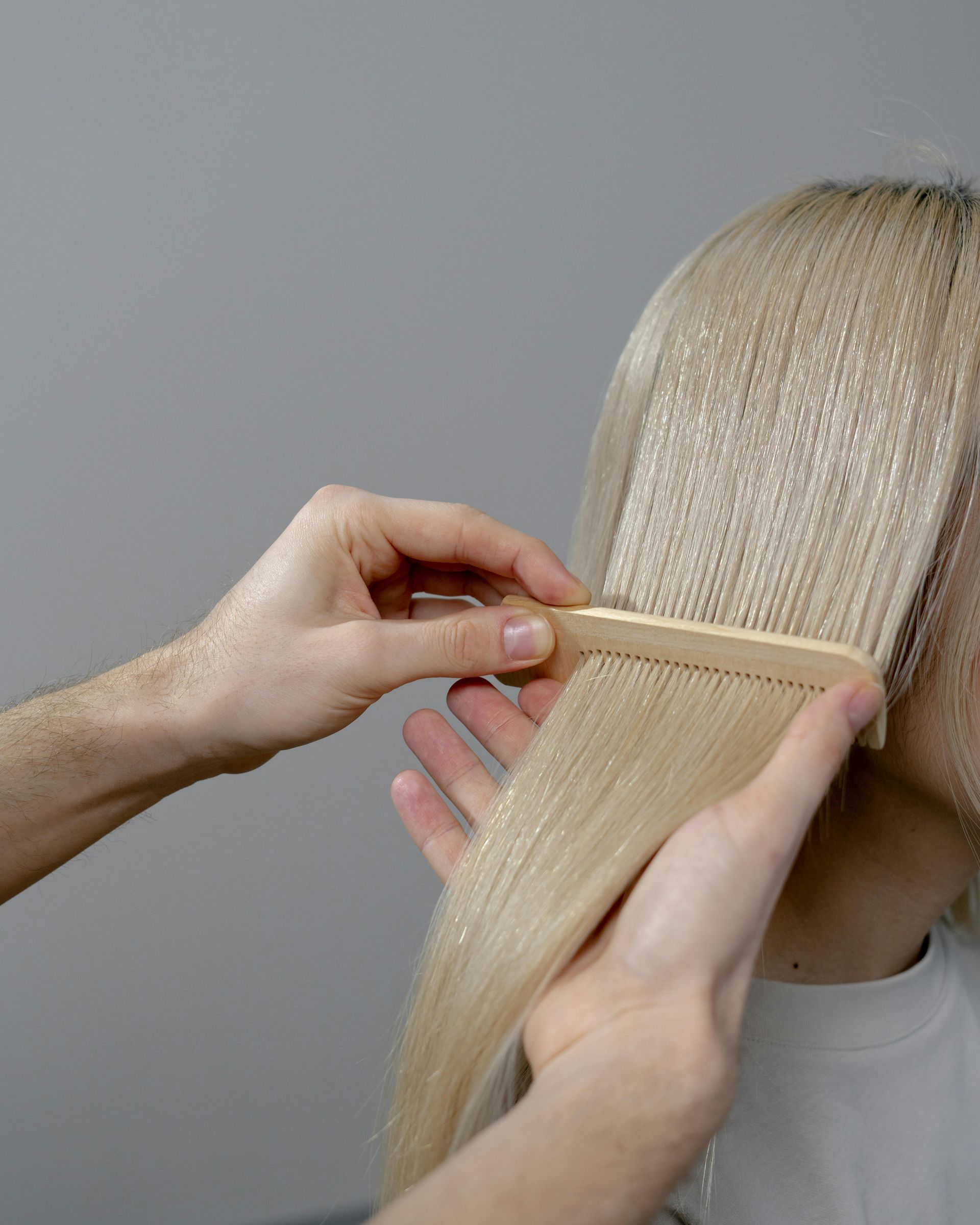 Person combing blonde hair with wooden comb.