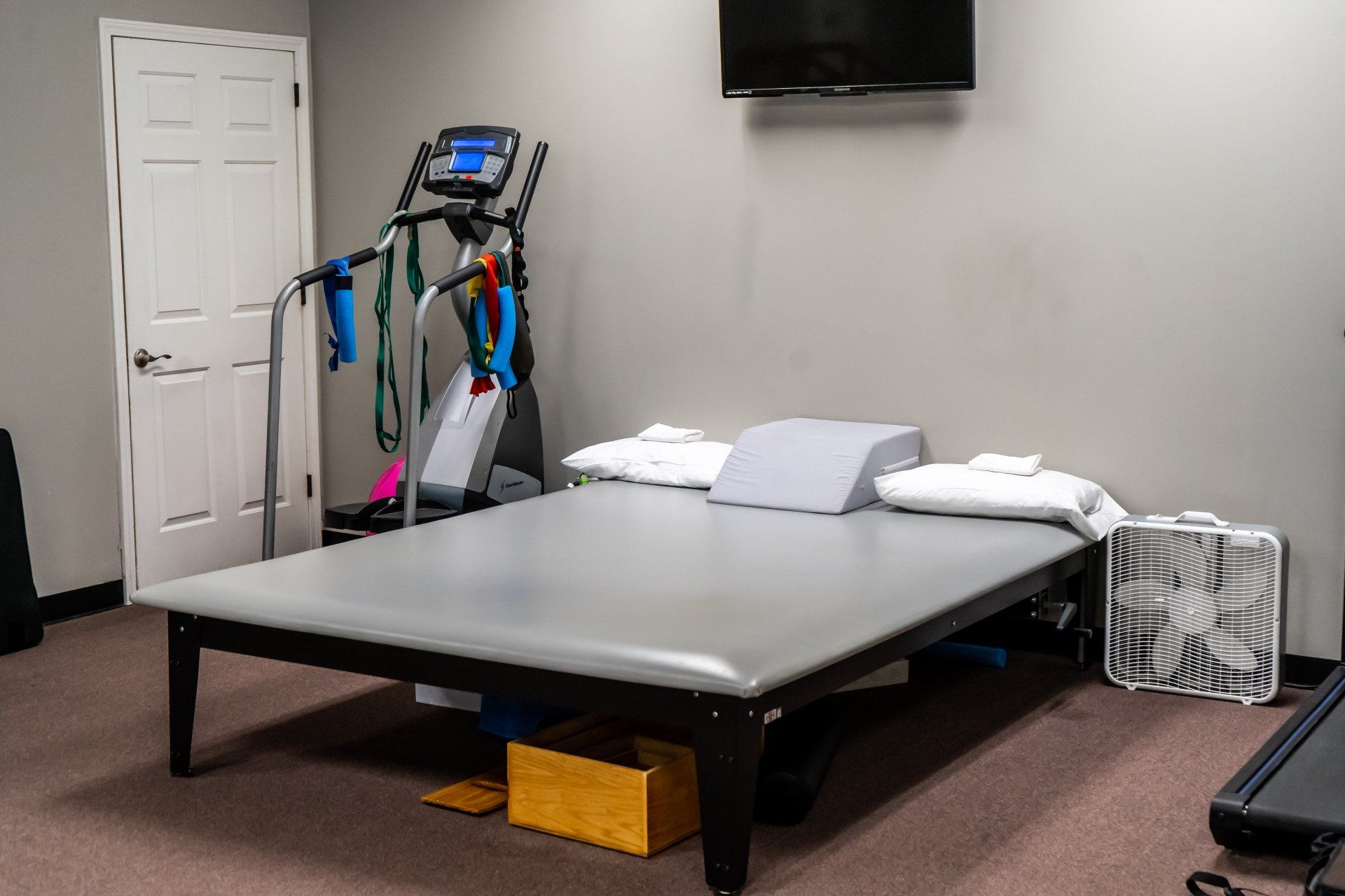 a therapy room with a bed , treadmill , fan and television .