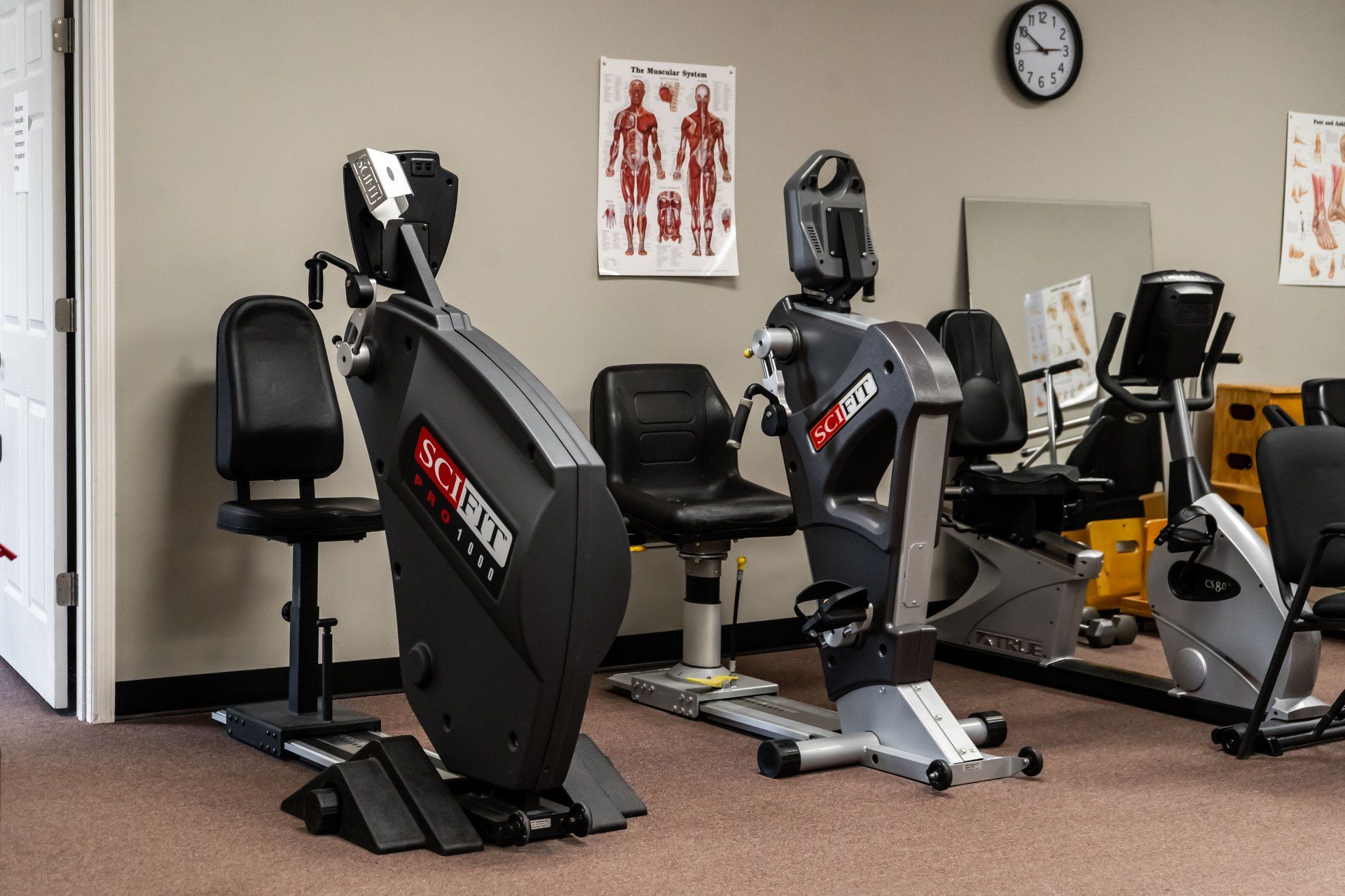 a room filled with exercise bikes and chairs and a clock on the wall .