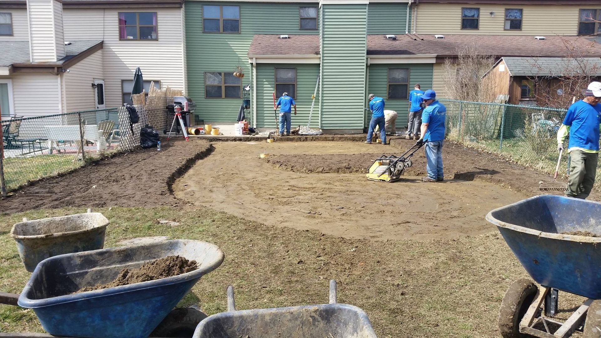 A group of people are working in a yard with wheelbarrows filled with dirt.