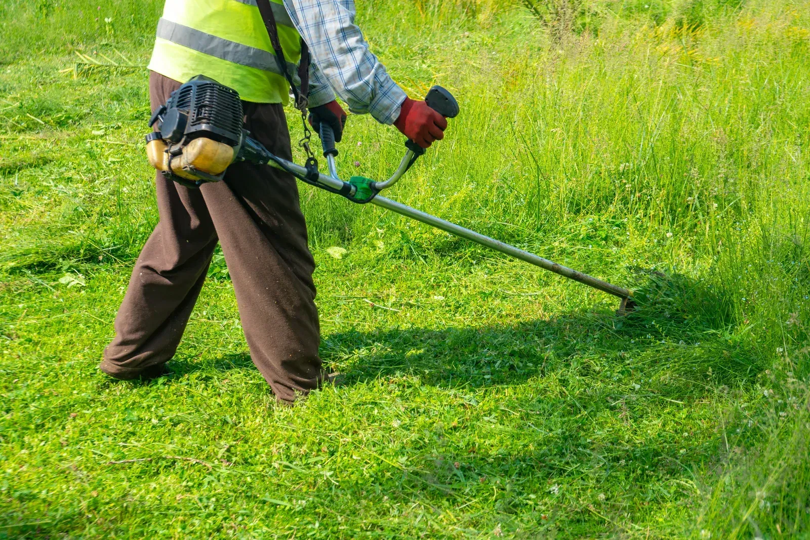 A man is cutting grass with a lawn mower in a field.
