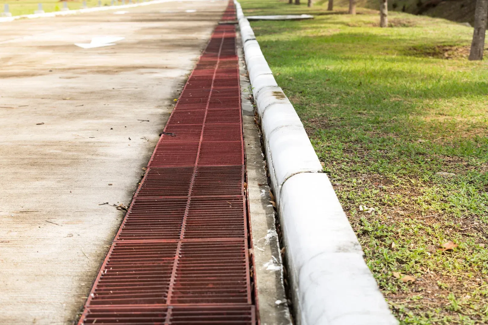 A drain on the side of a road next to a grassy area.