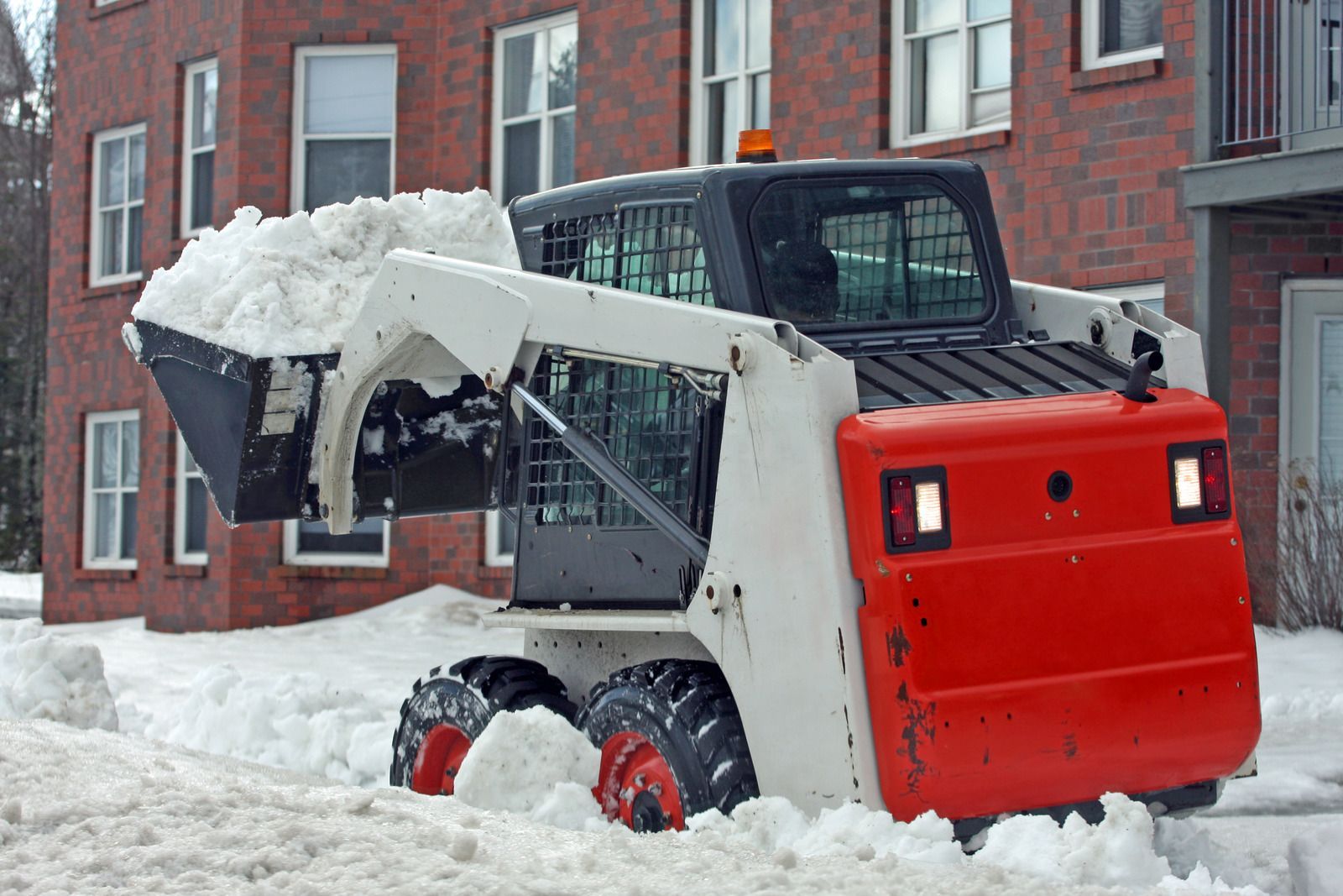 A snow plow is clearing snow from the sidewalk in front of a brick building.
