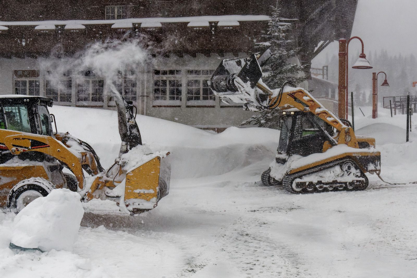 Two snow plows are clearing snow in front of a building.