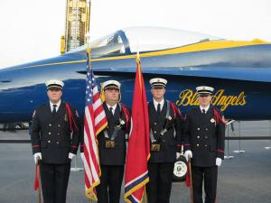 A group of men standing in front of a blue angels jet holding flags.