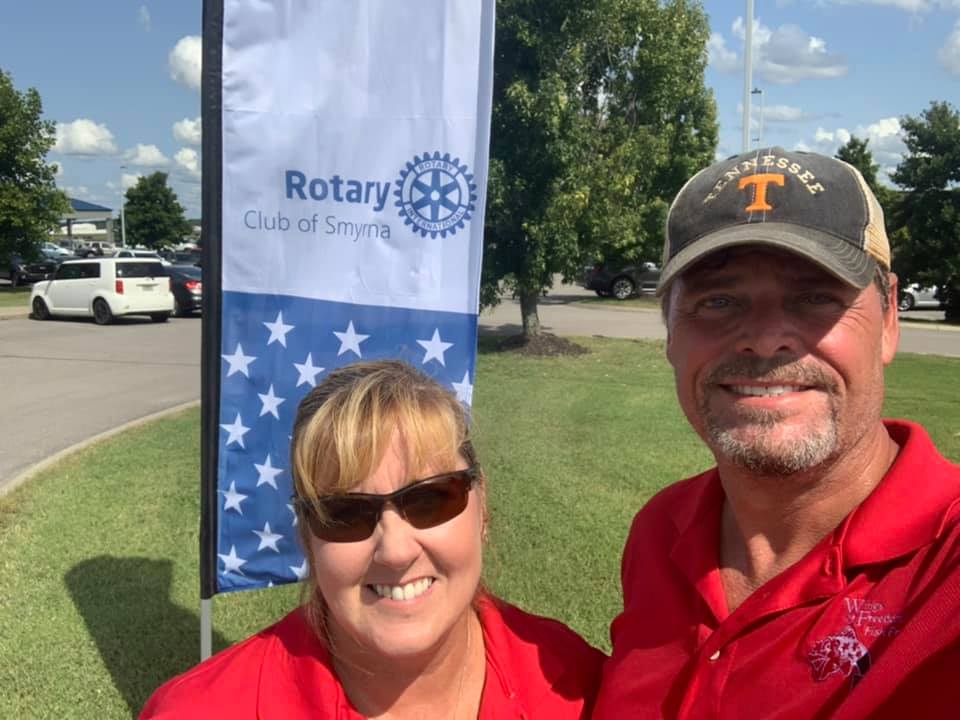 A man and a woman are posing for a picture in front of a rotary flag